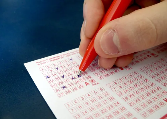 A hand fills in the numbers on a lottery slip.